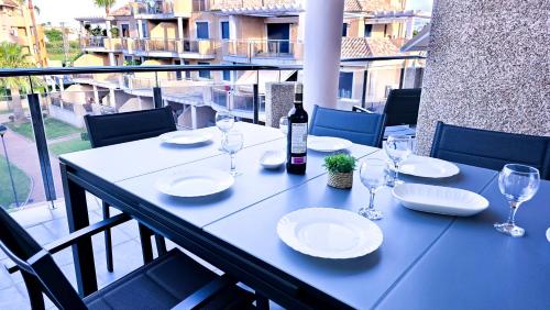 Mesa al aire libre con platos, copas y una botella de vino, situada en un balcón con vistas a un complejo de apartamentos.